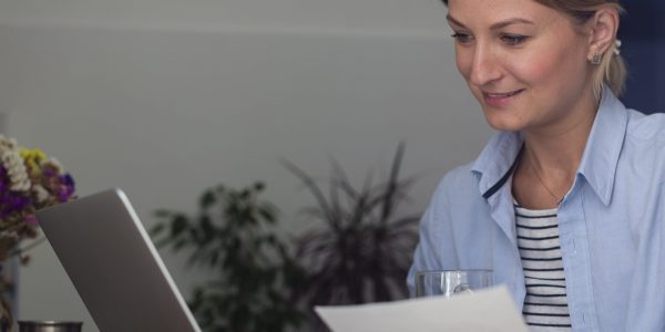 woman-holding-paper-looking-laptop-min